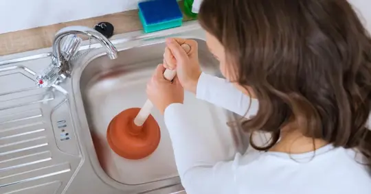 Woman using a plunger in the kitchen sink
